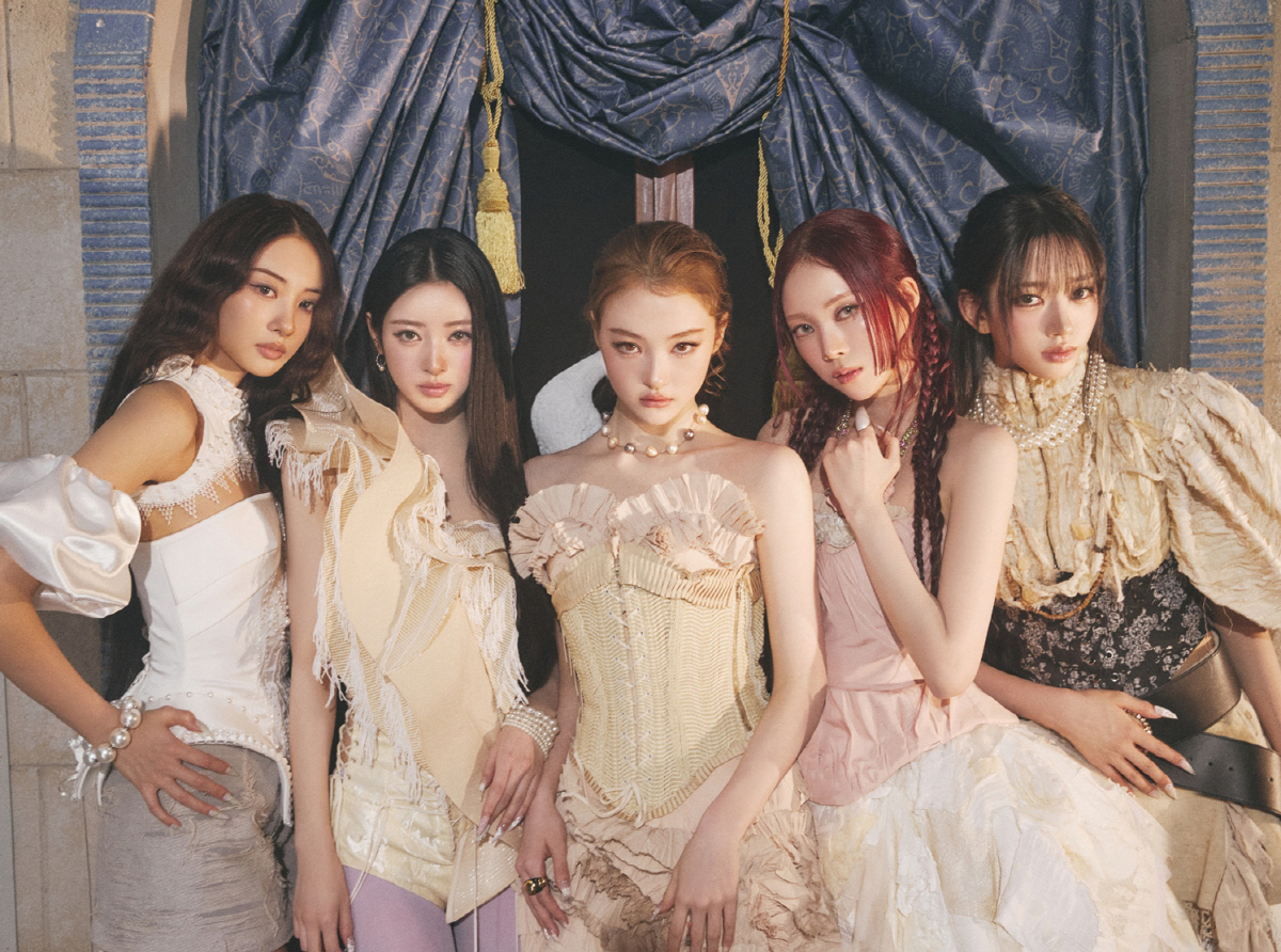 MEOVV members in pearl-trimmed corsetry and ornate court-inspired styling.